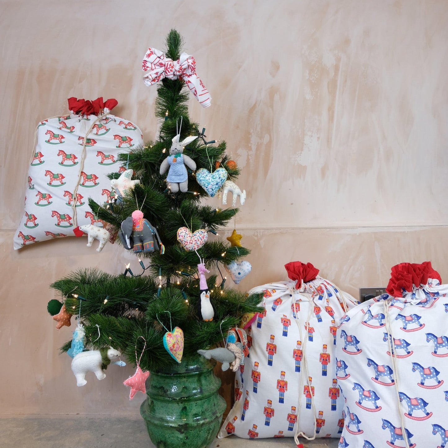 Small decorated Christmas tree with ornaments next to wrapped presents on a neutral background