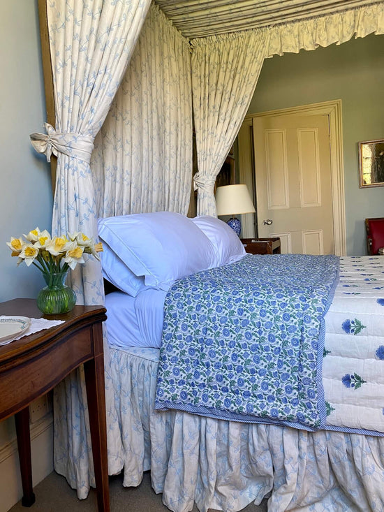 Blue flower pattern bespoke bed quilts with antique beside table with yellow daffodils