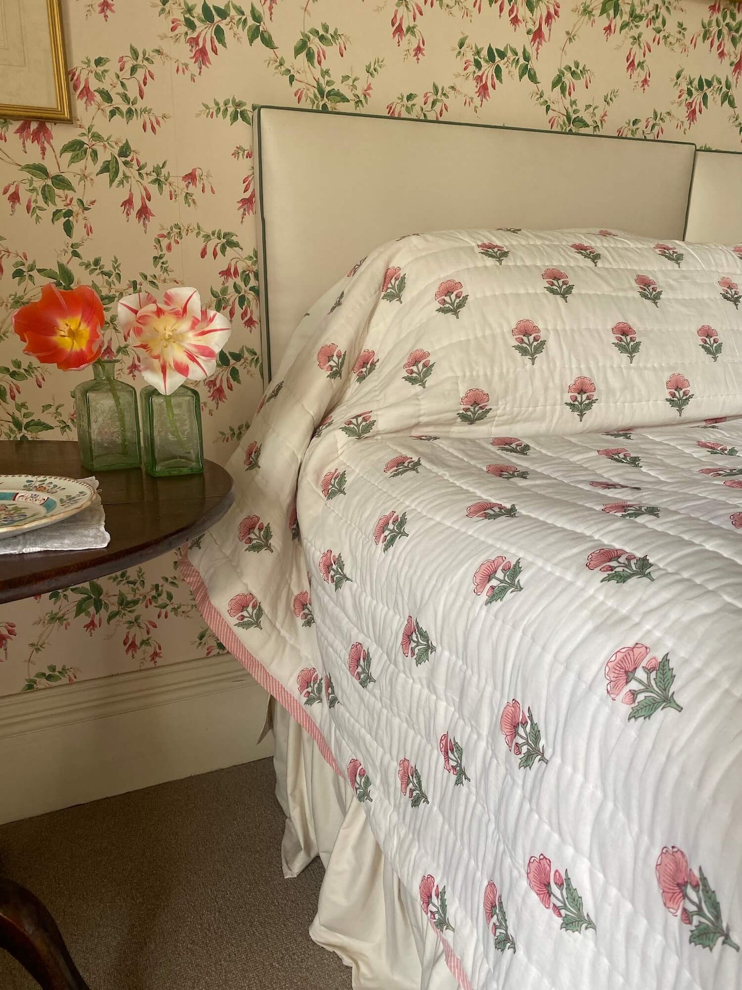Flower pattern bespoke bed quilts next to antique table with fresh flowers