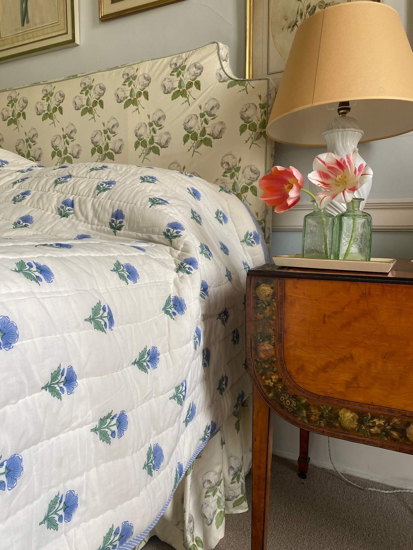 White and blue flower bespoke bed quilts next to antique bedsite table with fresh flowers and lamp