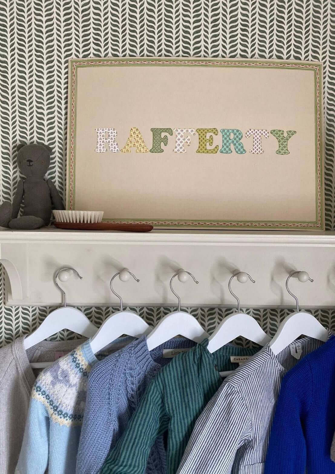 Bespoke name print that reads Rafferty, placed on top of a clothes hook with various children's knitwear on hangers